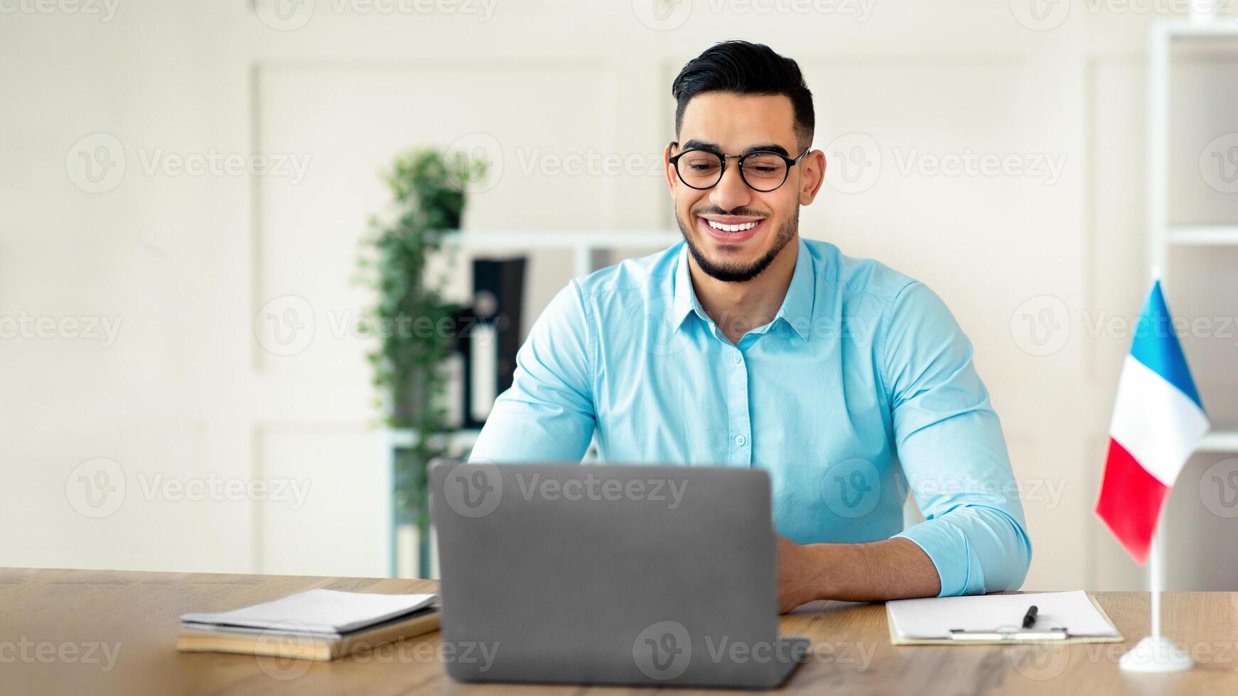 Online foreign languages tutoring. Cheerful Arab guy teacher giving French class, communicating on laptop from home. Experienced college professor giving new material to students on web photo