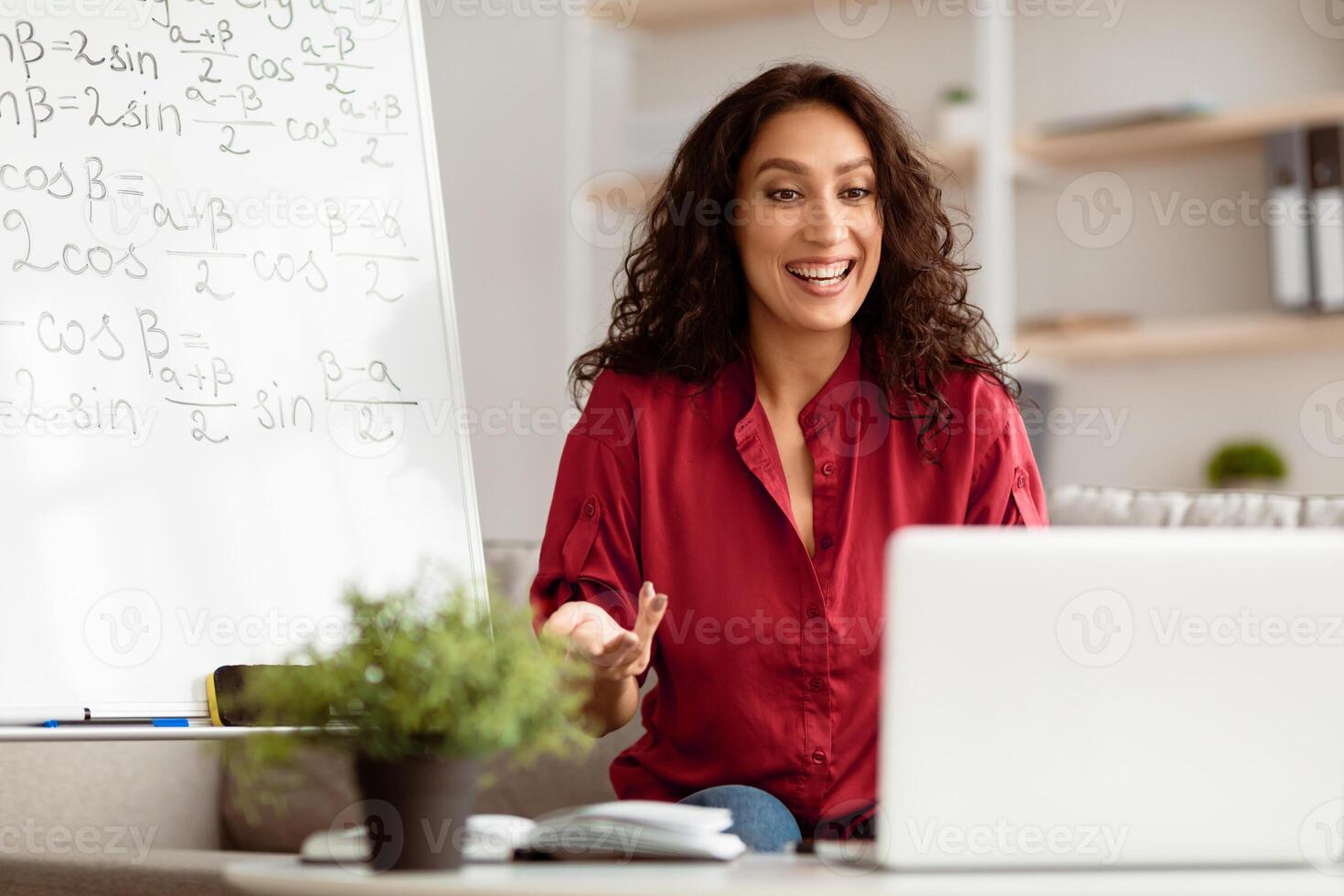 E-Learning Concept. Smiling lady math teacher talking, explaining trigonometric functions to students on videocall. Excited woman looking at laptop screen, sitting at desk photo