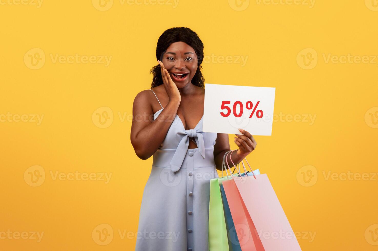 Good shopping, huge discounts concept. Happy young black woman holding gift bags, showing SALE sign, excited over her purchases, cannot believe special offer on orange studio background photo