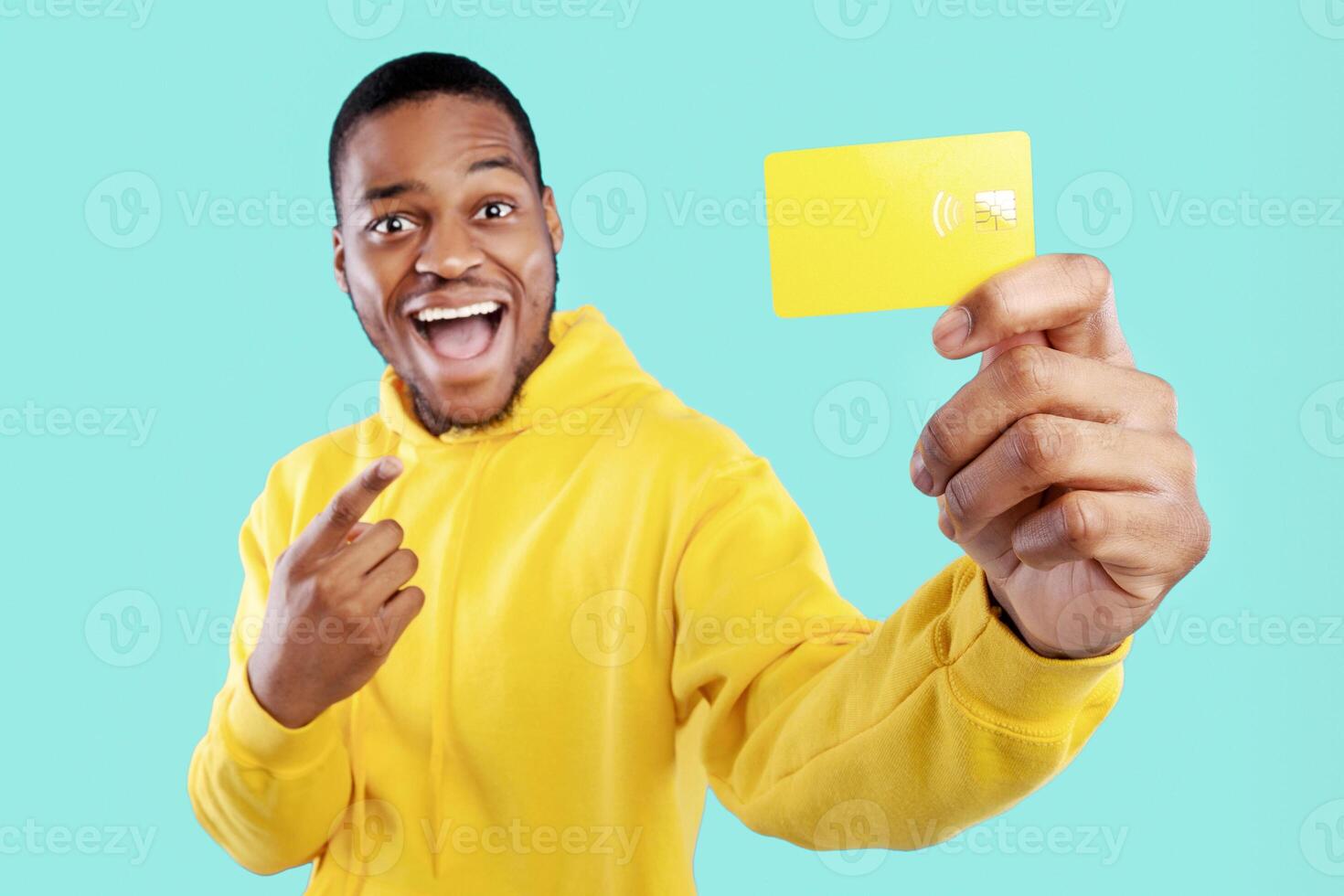 Excited Black Guy Showing Credit Card Pointing Finger Advertising Great Bank Service Posing Over Blue Background In Studio. Money And Finances, Look At This Concept. Selective Focus photo