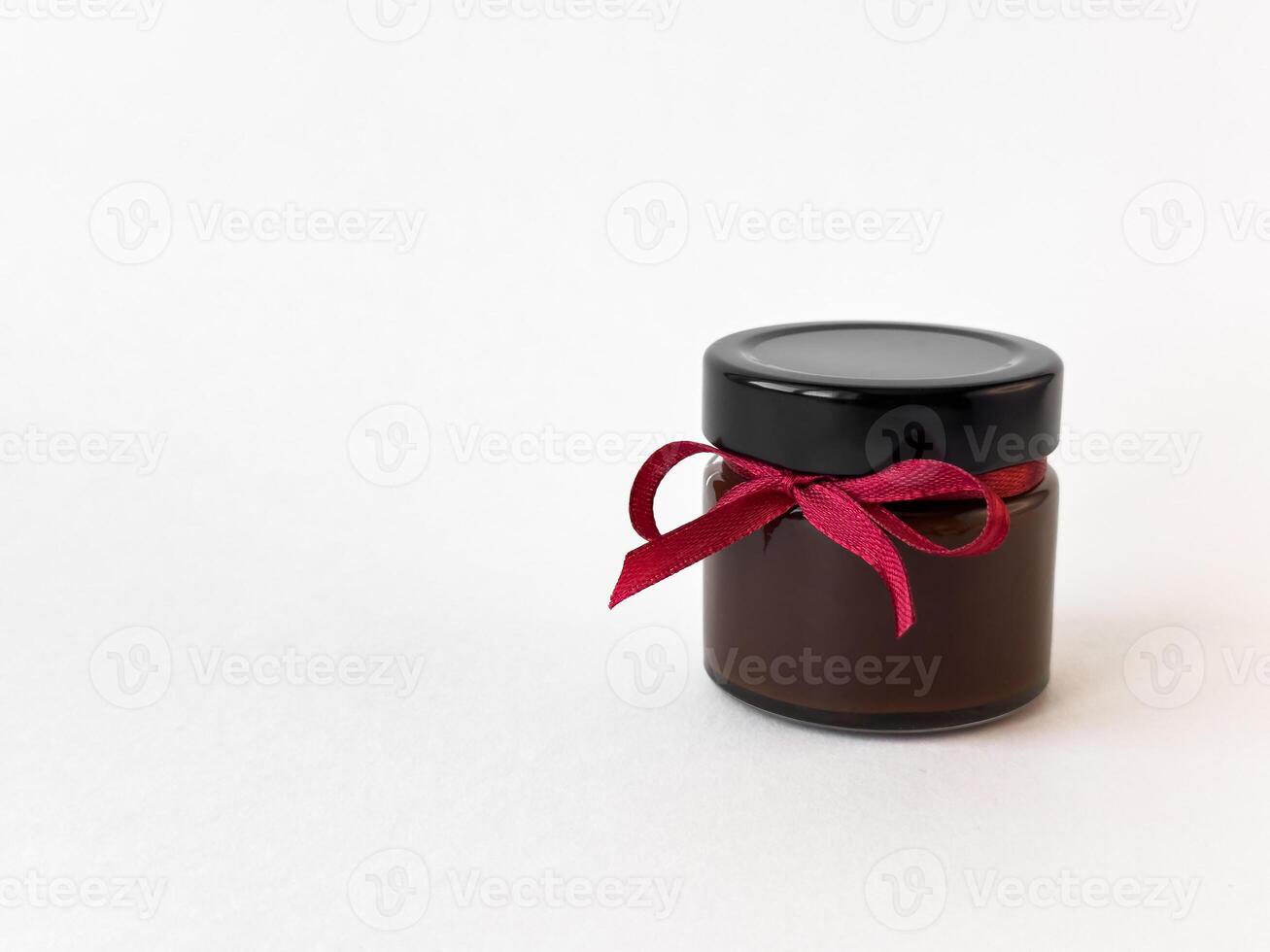 Elegant jar of chocolate spread tied with red ribbon on white background photo