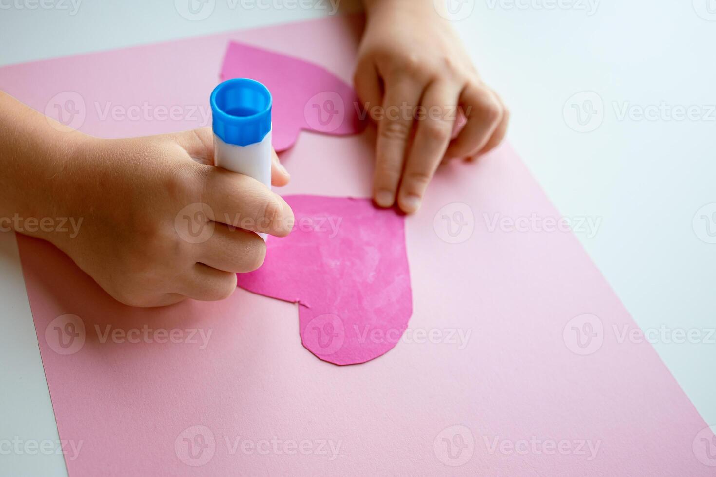 Child creating heart shaped crafts with pink paper and glue stick photo