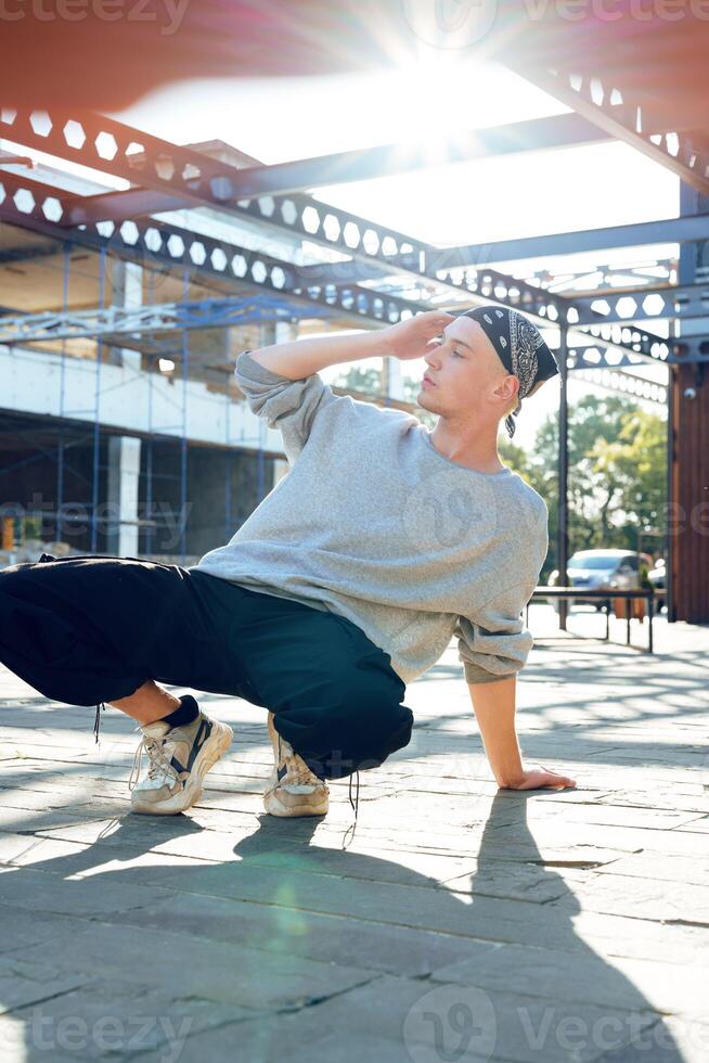 A young man in a grey sweatshirt and black pants practices breakdancing in front of a building under construction photo