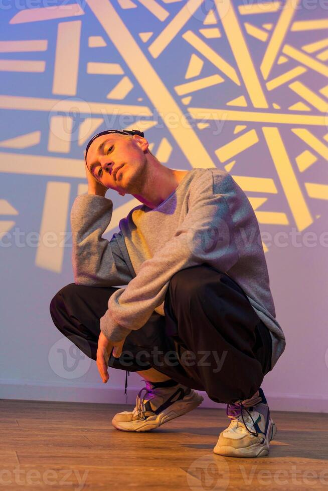A young man sits with his legs crossed in a squat, with a projection of white lines and shapes behind him photo