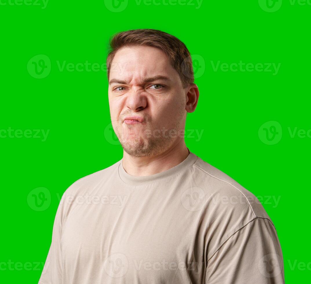Young man making a disgusted expression while standing against a bright green background photo