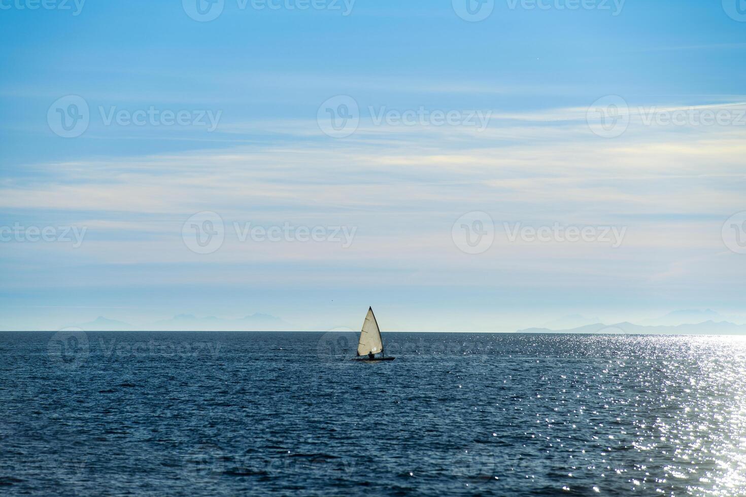 Small sailboat in backlight sailing in the ocean photo