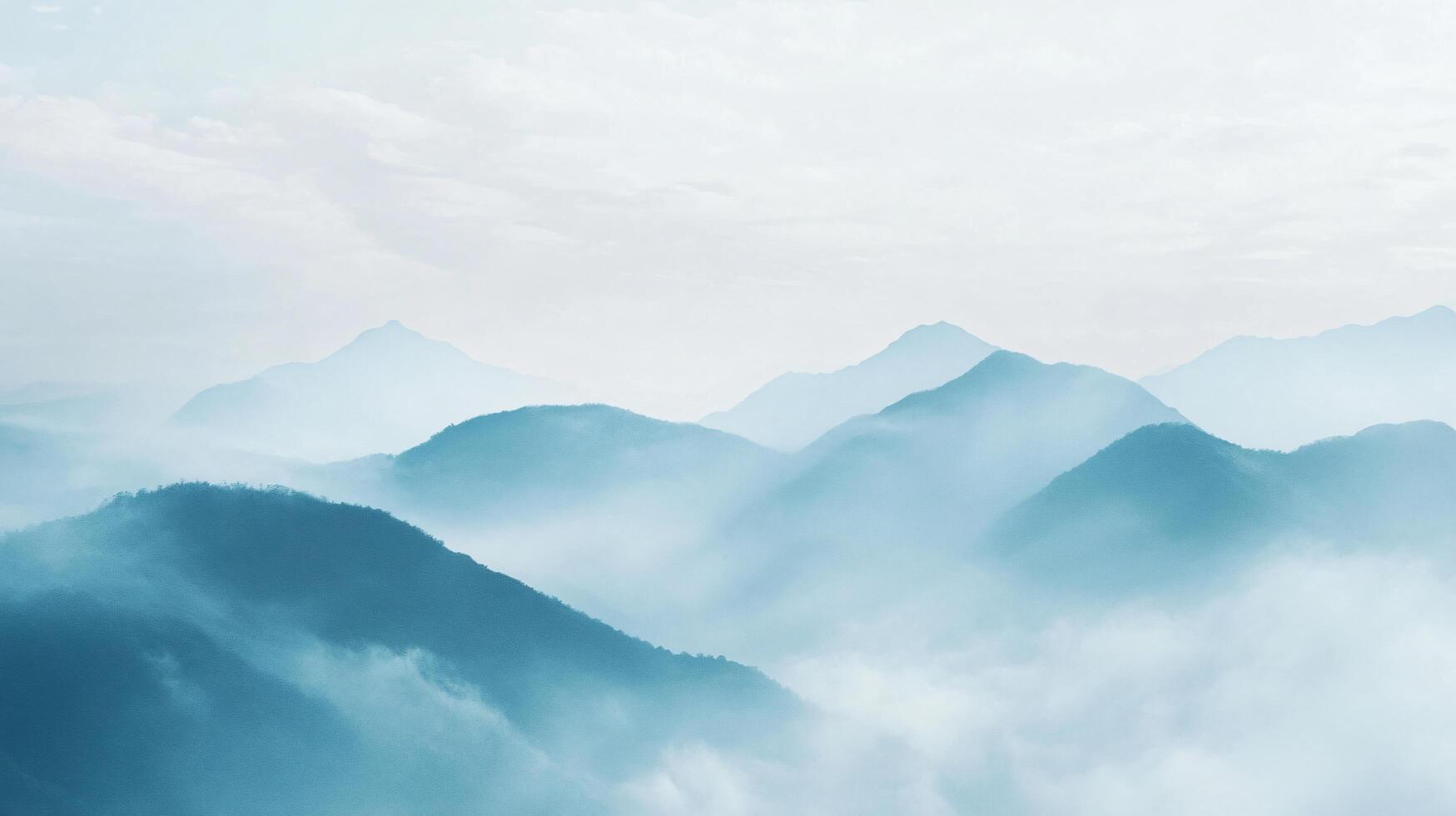 Low lying fog blankets a mountain range, creating a serene, blue toned landscape under a soft cloudy sky photo