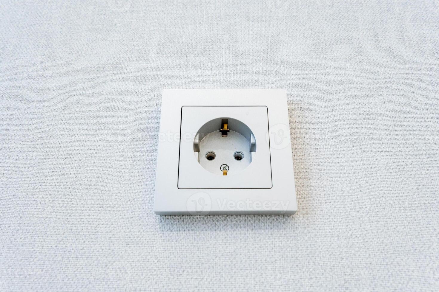A rectangular metal wall socket blending in with the white wall photo