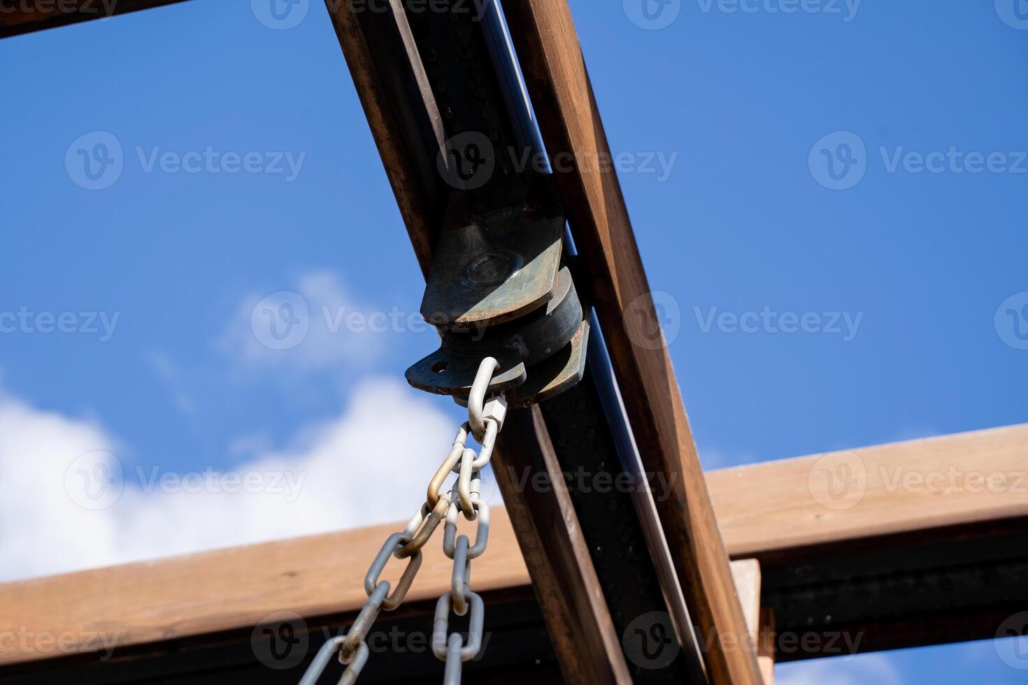 A detailed closeup image showcasing a metal pulley and chain set against a beautiful blue sky, capturing intricate architectural elements photo