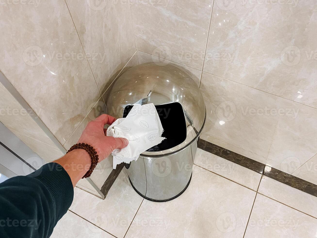 Utilizing a fluid motion, someone disposes a paper into a bathroom trash can made of composite materials. photo