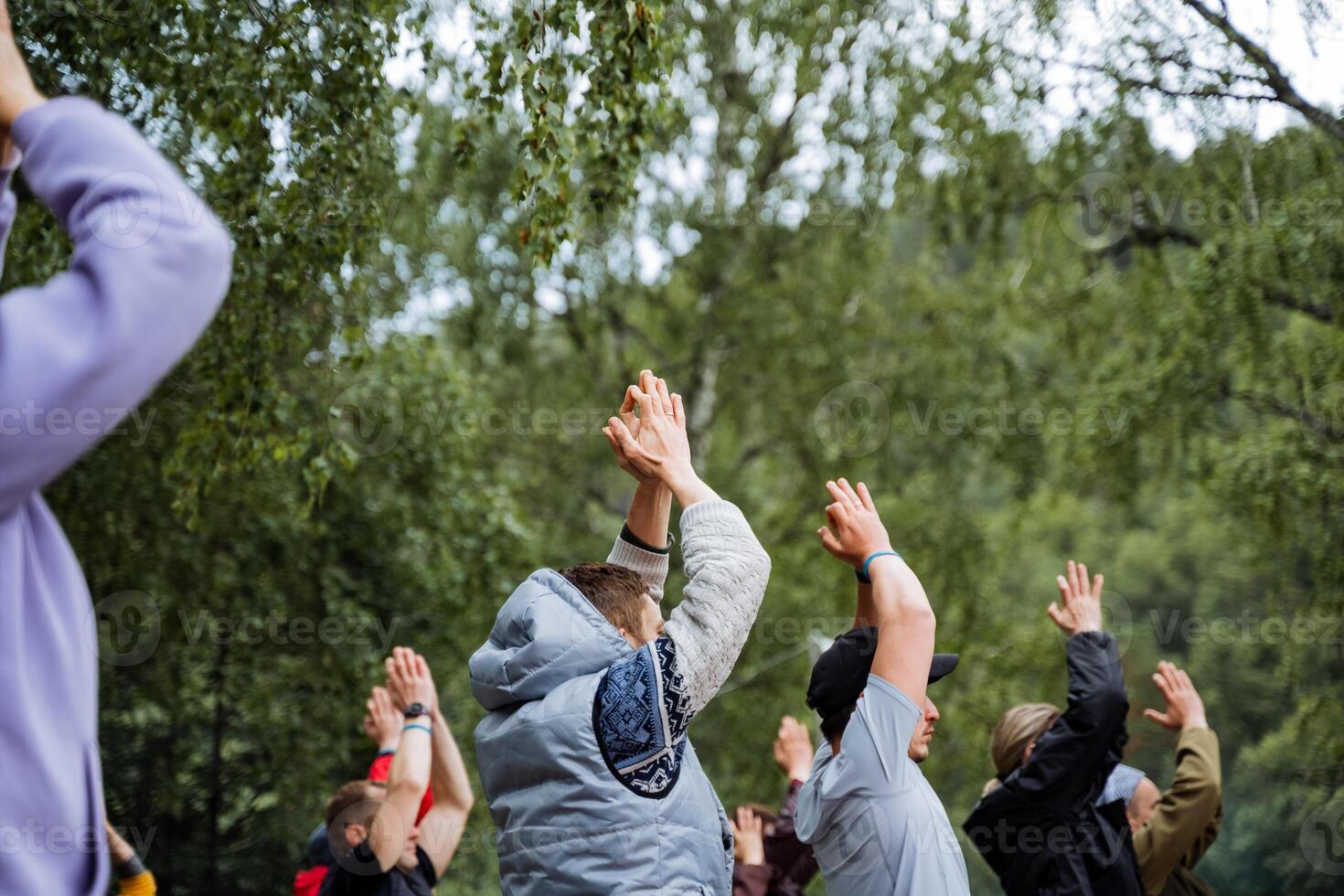 A group of people is seen engaging in outdoor recreational activities in a circle, raising their hands in the air. They seem to be having a good time in a natural setting photo