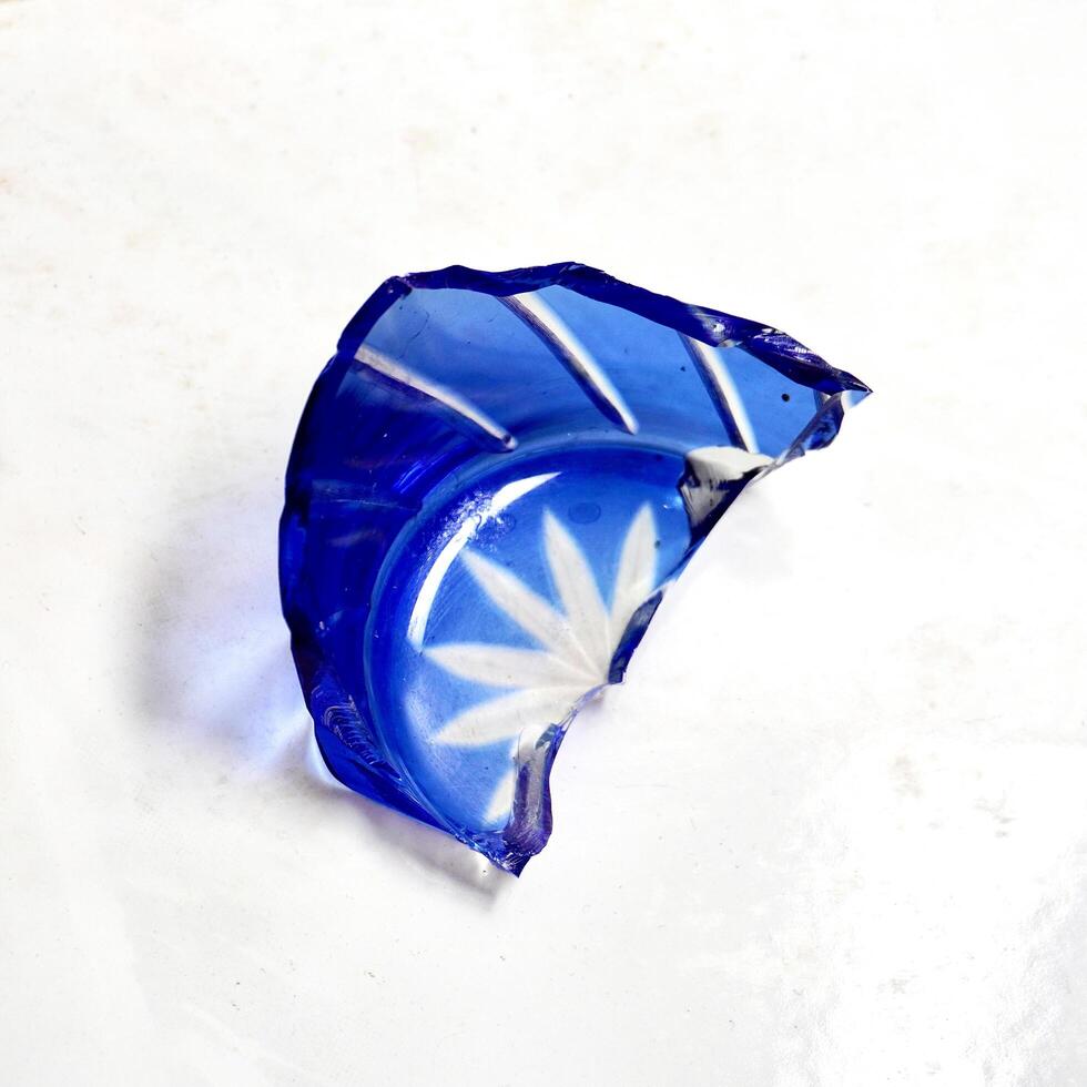 One piece of broken blue glass drinkware with sharp fragment edges isolated on square white floor background. photo
