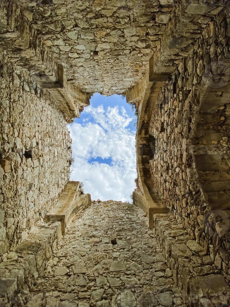 A sturdy stone wall with a beautifully designed window offers a breathtaking view of the blue sky, inspiring reflections on the rich history and charm of the ancient ruins photo