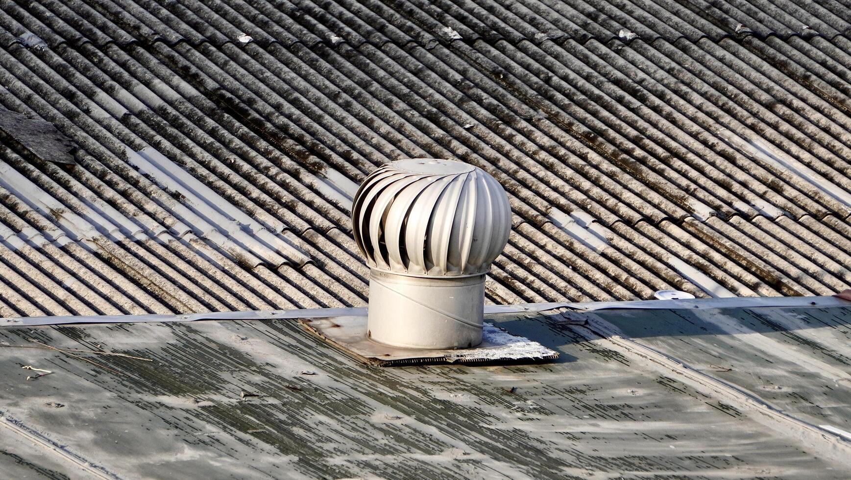 Round metal turbine ventilator system building exterior object isolated on horizontal asbestos roof background. photo
