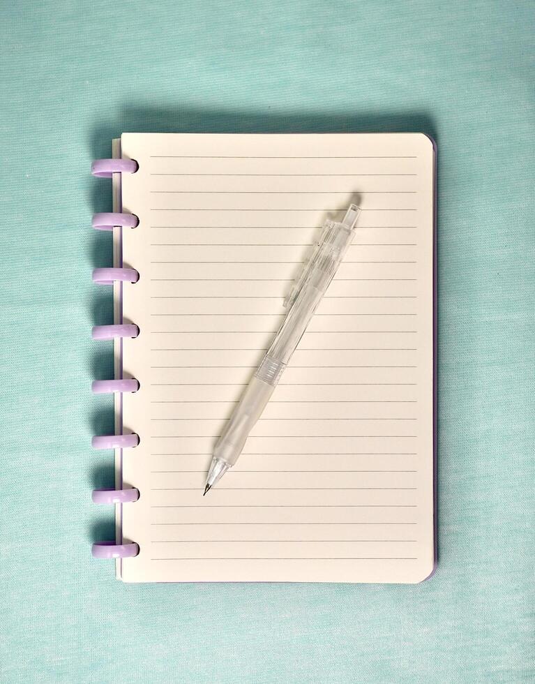 Note book with white lined paper and purple spiral spine and mechanical pencil above the paper isolated on vertical light blue background. photo