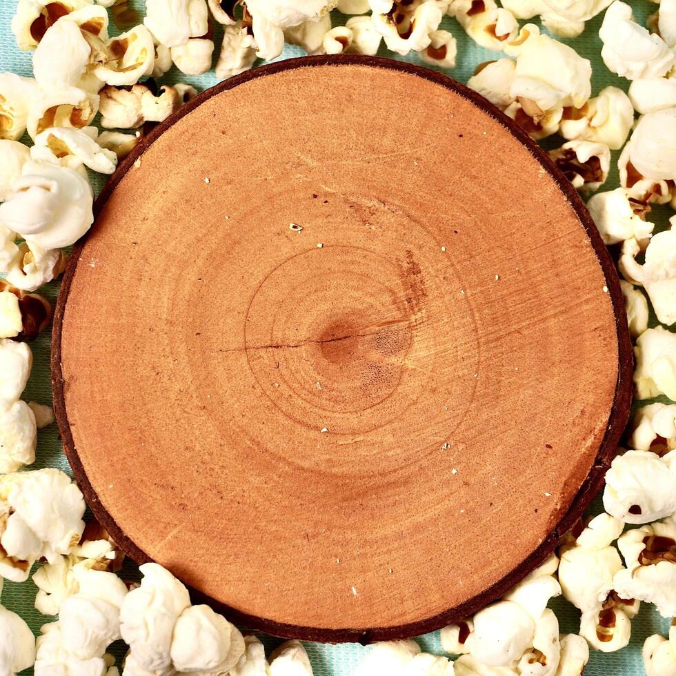 Crunchy salted pop corn snack with round wooden coaster platform copy space isolated on square background. photo