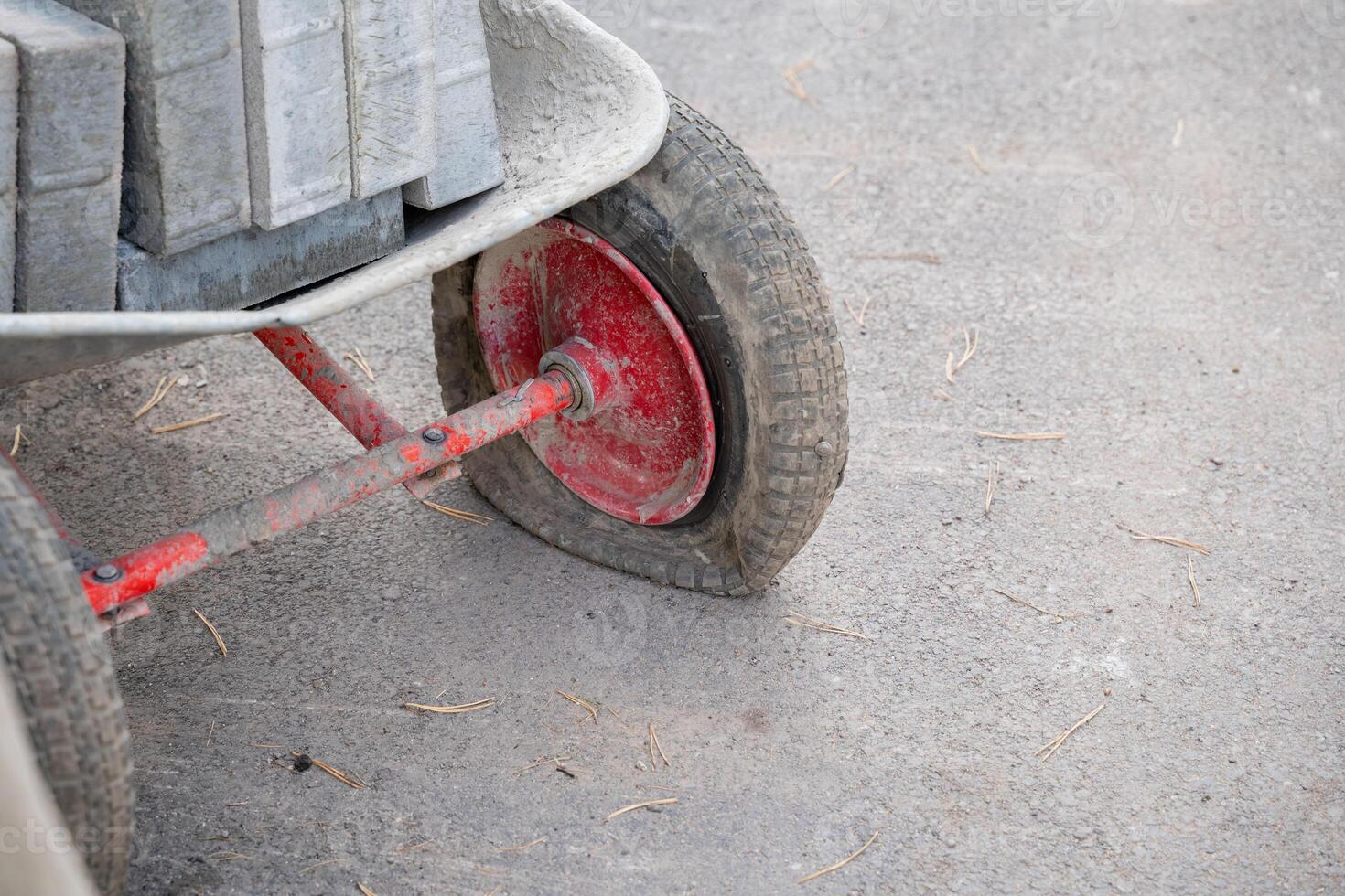 At a busy construction site, a cart that is filled with heavy concrete blocks has a flat tire, which is leading to a delay in the ongoing work photo