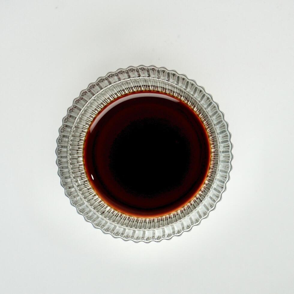 Brown soy sauce condiment and seasoning for sushi in small glass bowl from top angle view isolated on square white background. photo