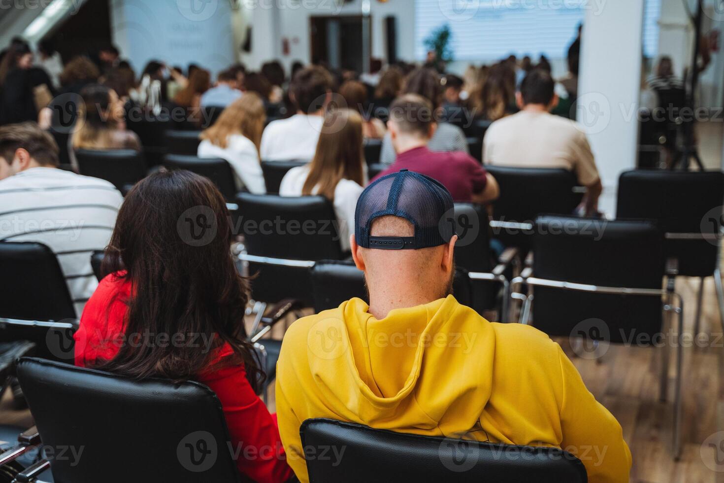 A man in a yellow hoodie is seated in front of a crowd at a community event photo