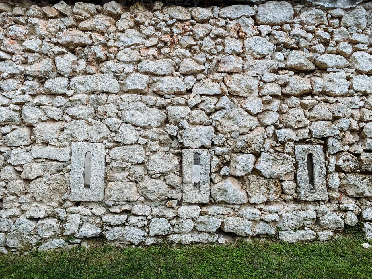 A sturdy stone wall that features a few noticeable holes within its structure, offering a glimpse into the materials used and the passage of time on this building barrier photo