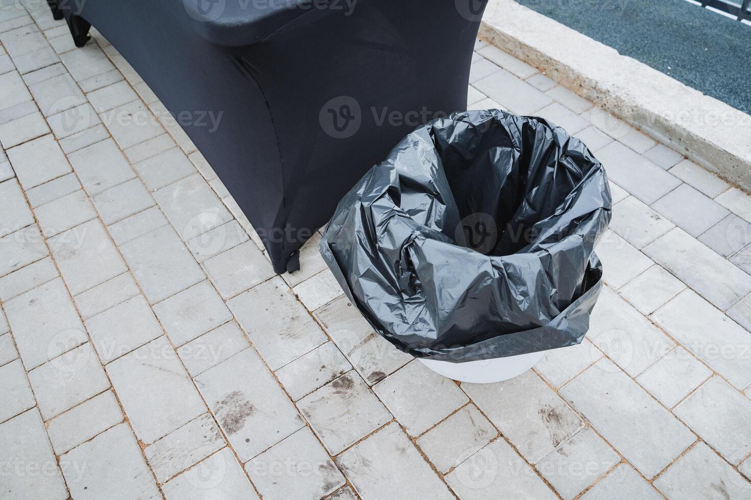 A black trash bag next to a sturdy wooden table highlights the contrast between waste and functionality in an outdoor setting, showcasing discarded items versus functional furniture photo