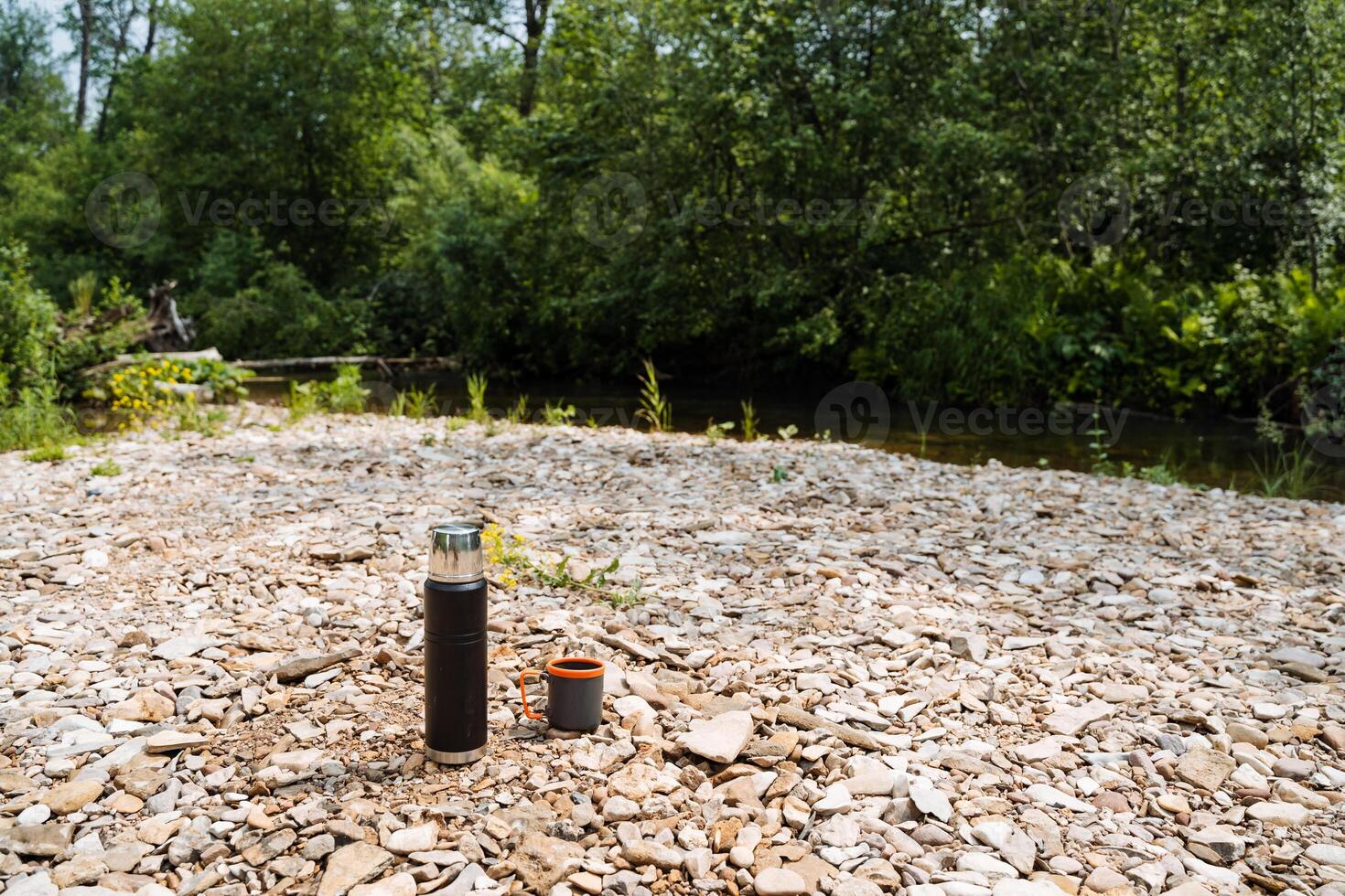 Near the tranquil river, a bottle and cup lay on the ground, blending seamlessly with the natural landscape. They are part of the peaceful environment, harmoniously coexisting with nature photo