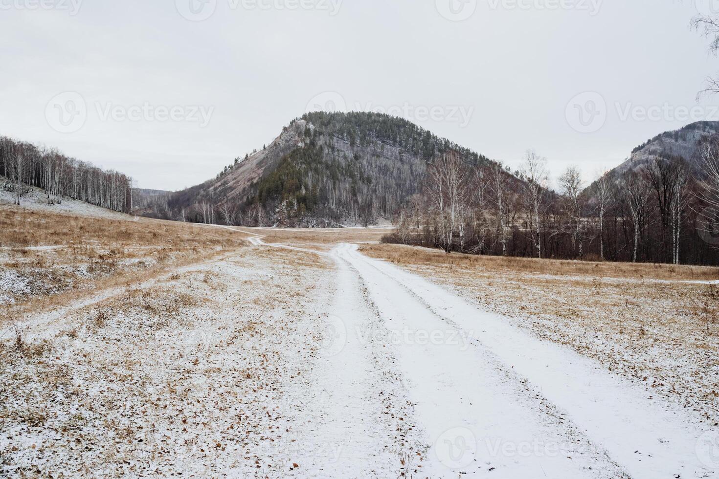 A rugged dirt road winds its way through an expansive snowy field, while majestic mountains rise prominently in the background, creating a breathtaking and stunning natural landscape photo