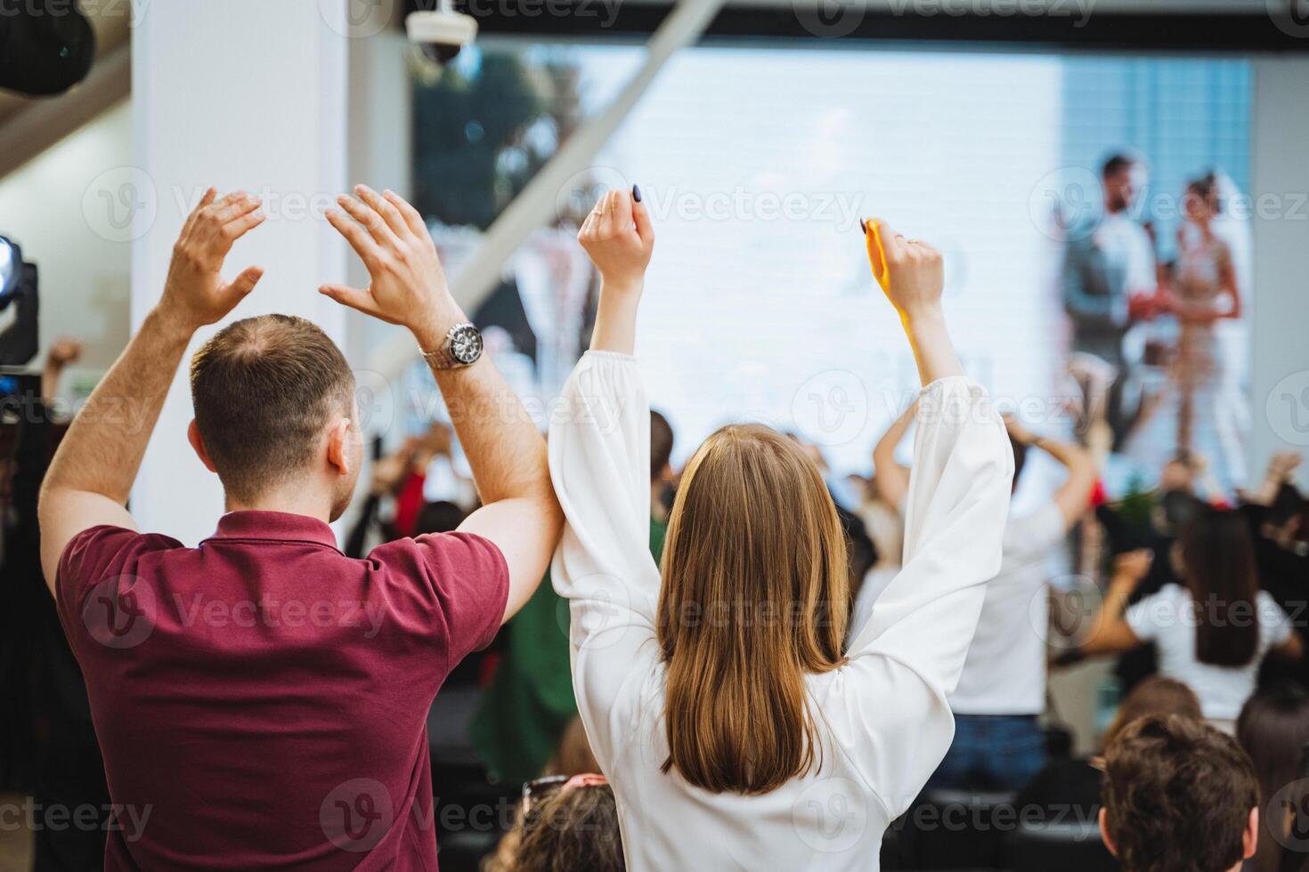 Crowd at an event making joint gesture in front of large display device photo