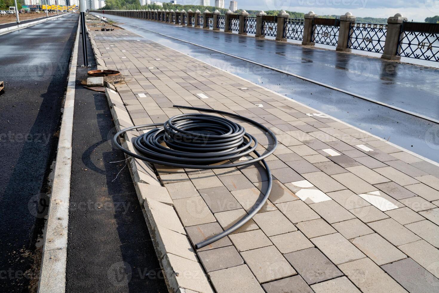 A vibrant garden hose is casually sprawled across the sidewalk next to a bridge, crafting a lively scene that beautifully illustrates the intersection of nature and urban infrastructure photo