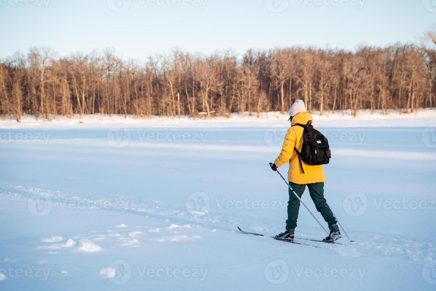 A man in a yellow jacket is skiing across snowy terrain under the sky photo