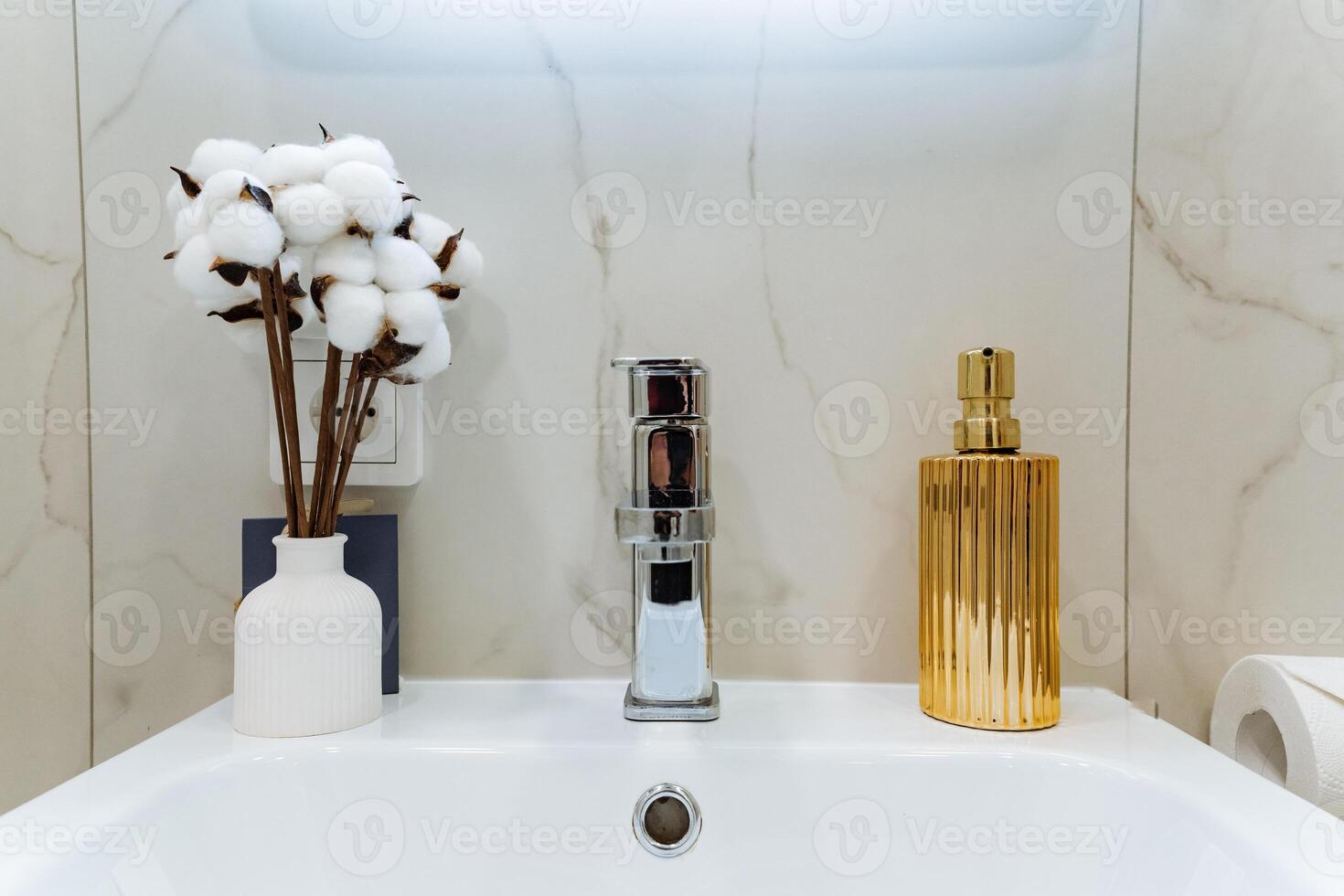 In a stylish bathroom, there is a lovely sink alongside a vibrant vase filled with beautiful cotton flowers and a welldesigned soap dispenser for added convenience and elegance photo