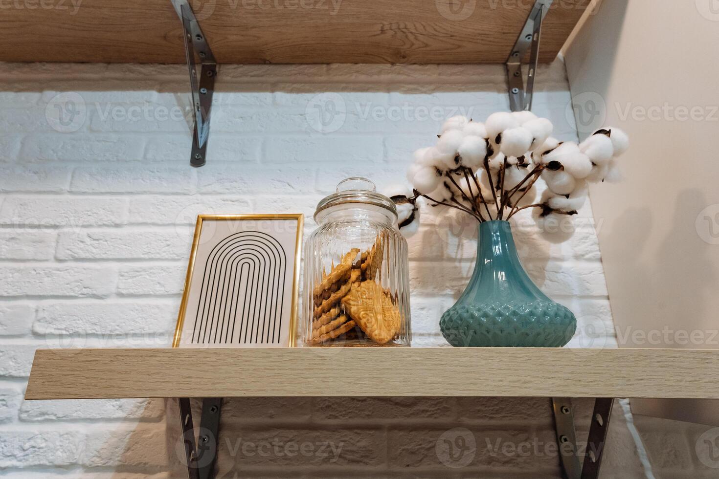 On a sturdy shelf, there sits a beautifully arranged vase filled with delicate cotton, alongside a charming jar full of delicious cookies, adding a cozy touch to any space photo