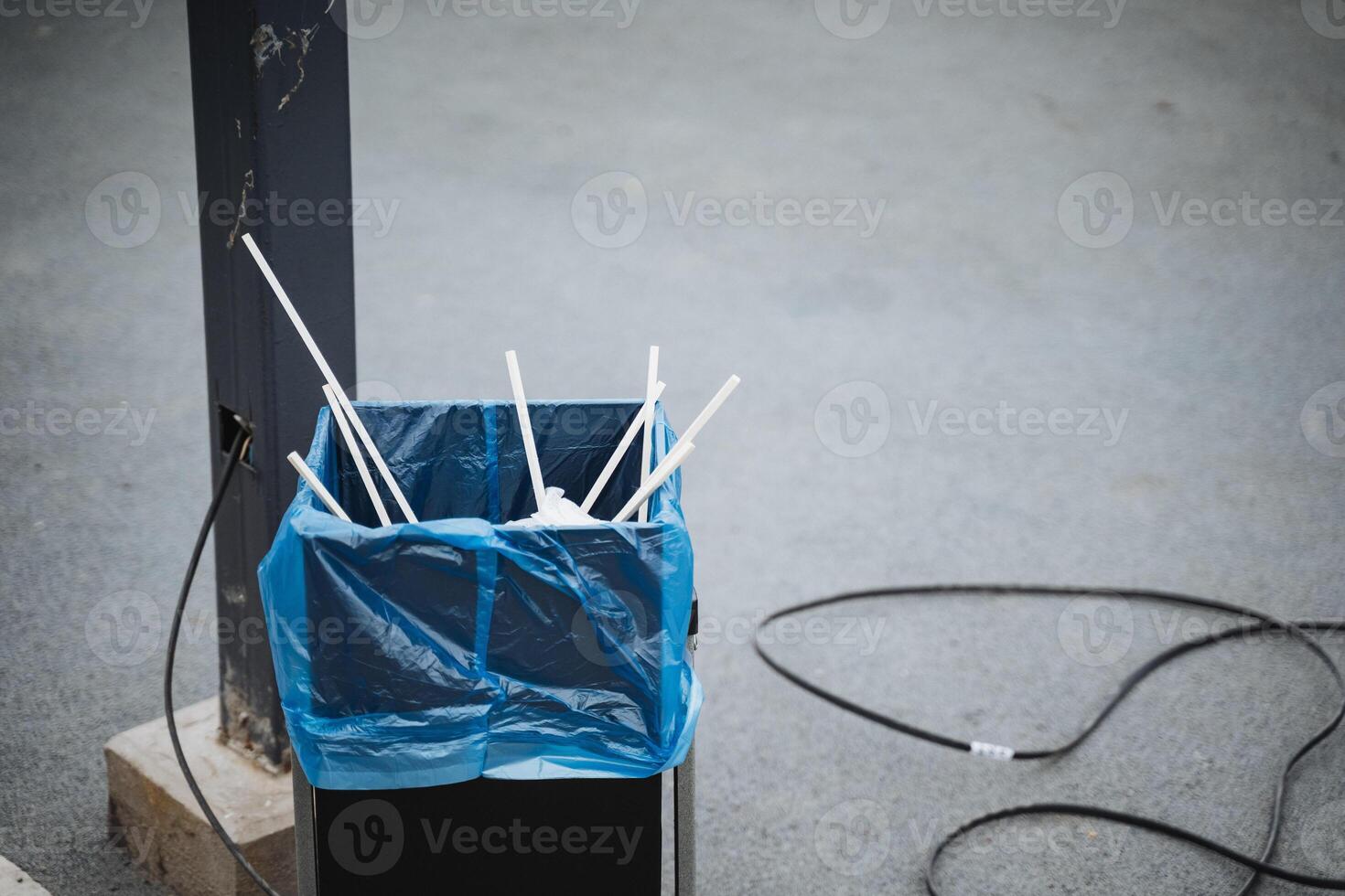 A trash can overflowing with discarded straws rests beside a sturdy pole, creating an interesting visual juxtaposition in this urban setting, showcasing materials like plastic and metal photo