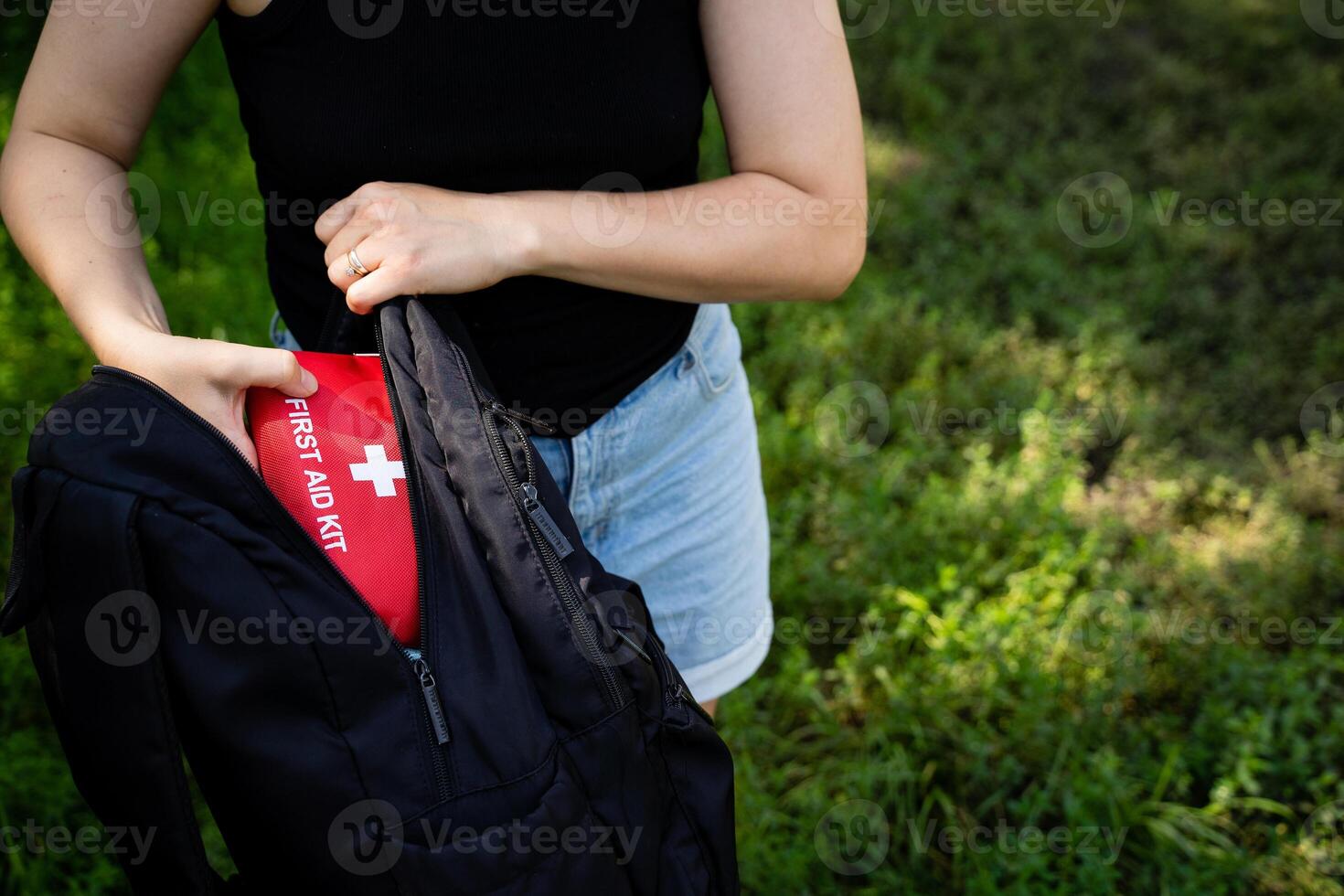 A woman is carefully placing a first aid kit into her backpack, ensuring she has all the necessary supplies for her journey ahead in case of any emergencies along the way photo