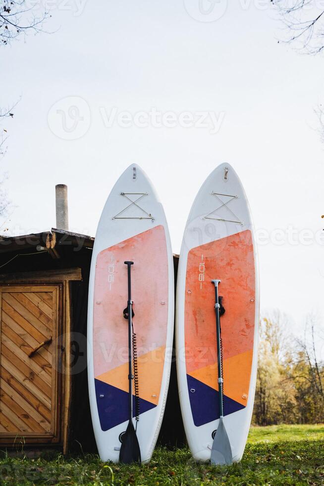 In a beautiful and picturesque setting, two surfboards, each thoughtfully equipped with sturdy oars for effective paddling, are casually leaning against a charming rustic wooden shed photo