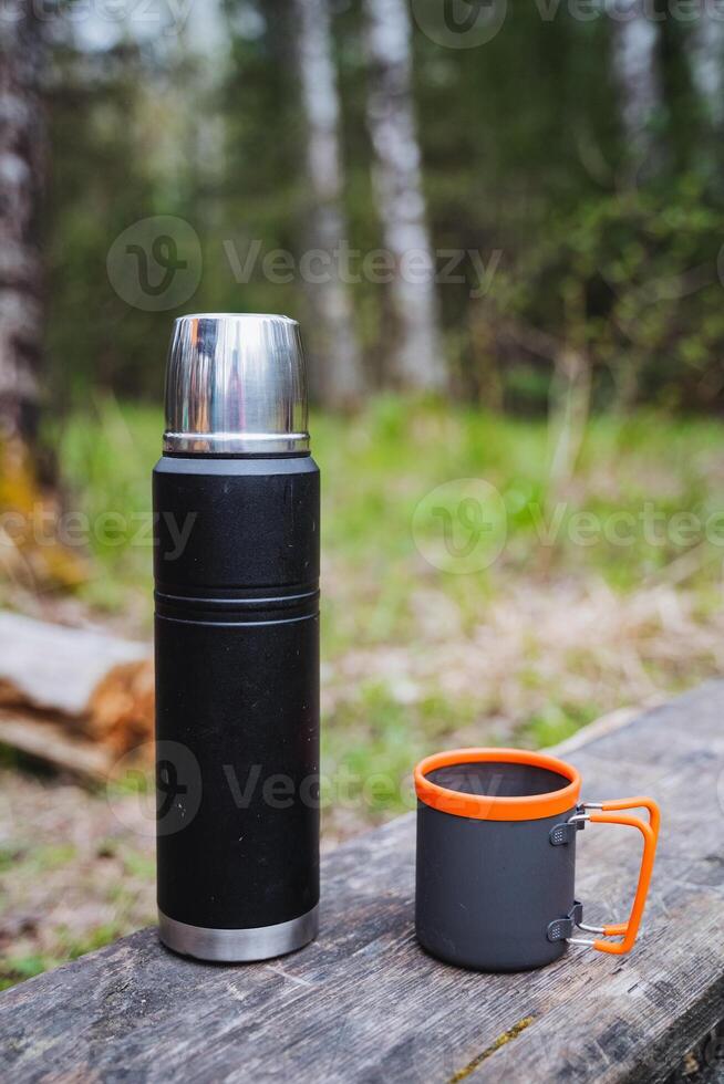A thermos and a mug are sitting on a wooden table photo