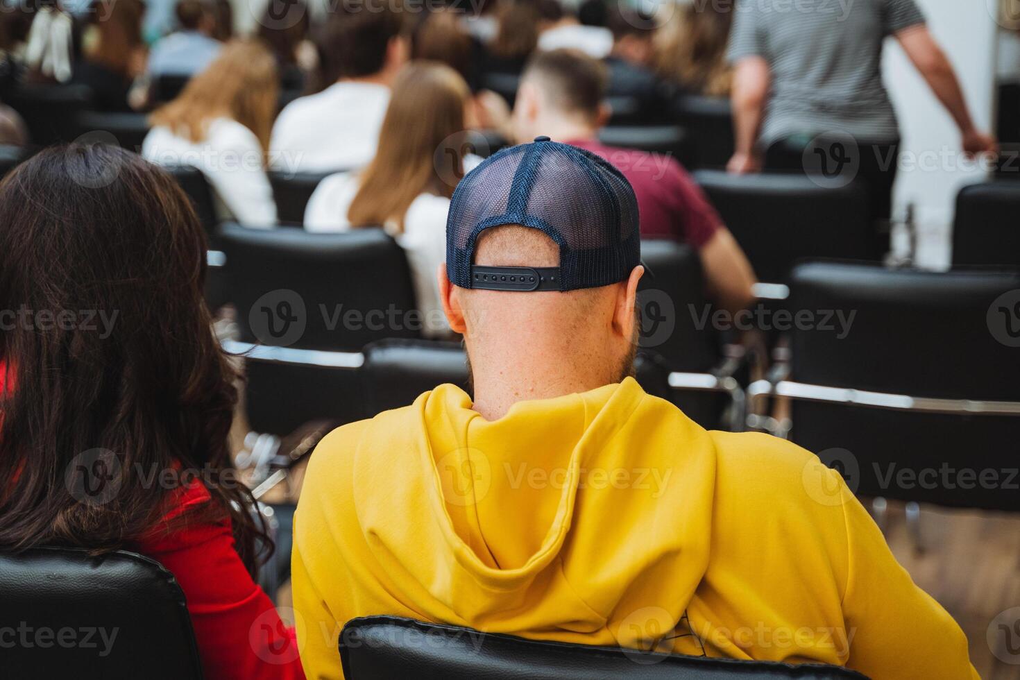 a man in a yellow hoodie is sitting in a chair in front of a crowd of people photo