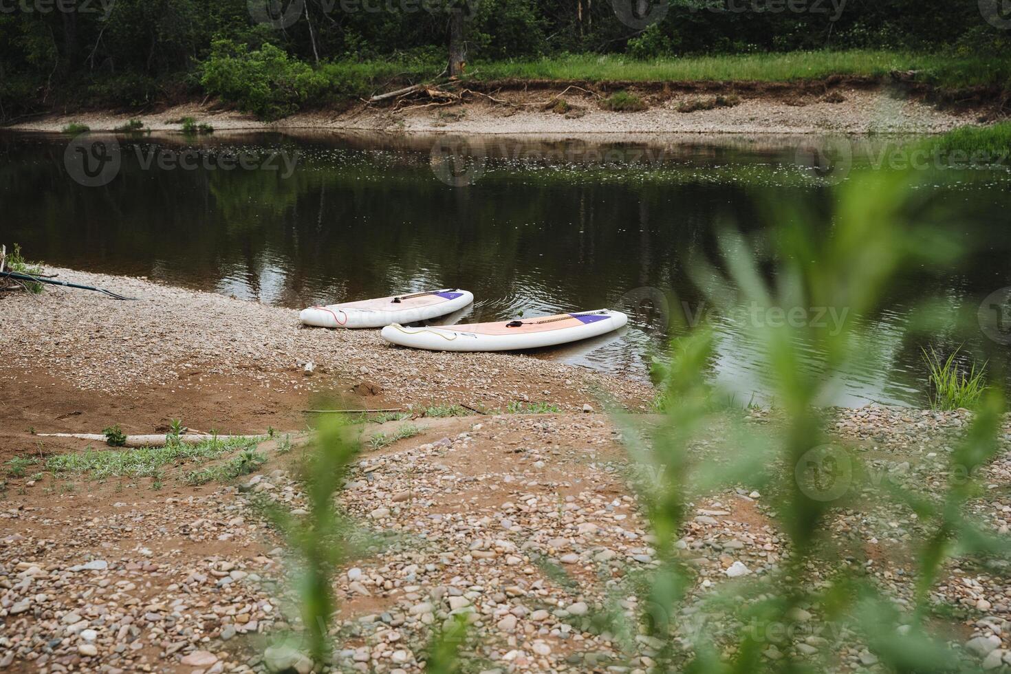 Experience a tranquil riverside view with paddleboards on the peaceful shore, surrounded by nature and calm waters, ideal for outdoor fun and relaxation in summer photo