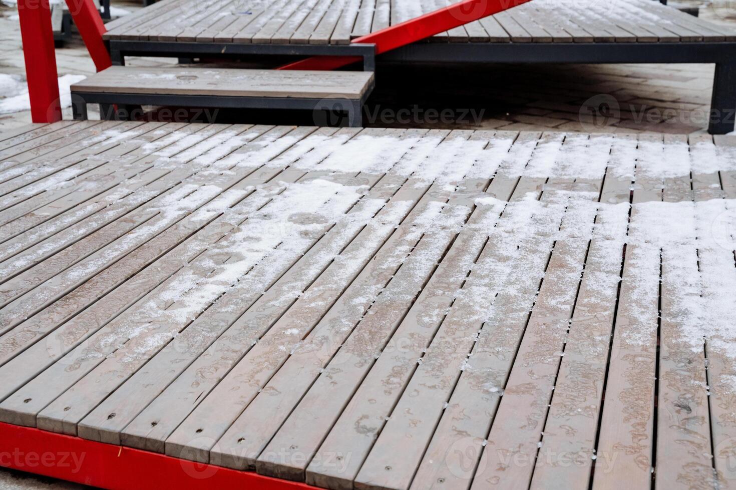 A stunning wooden deck, adorned with soft snow, features a vibrant red railing that contrasts beautifully with the pristine white snow, creating a picturesque winter scene photo