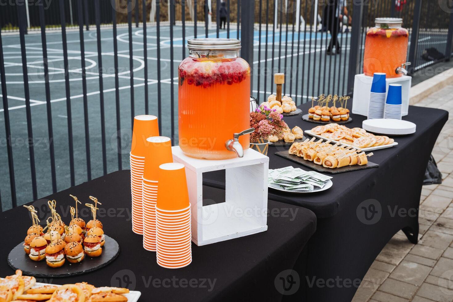 On the table, there is a drink dispenser filled with refreshing beverages, accompanied by an assortment of cups ready to be filled. Its perfect for any gathering or event photo