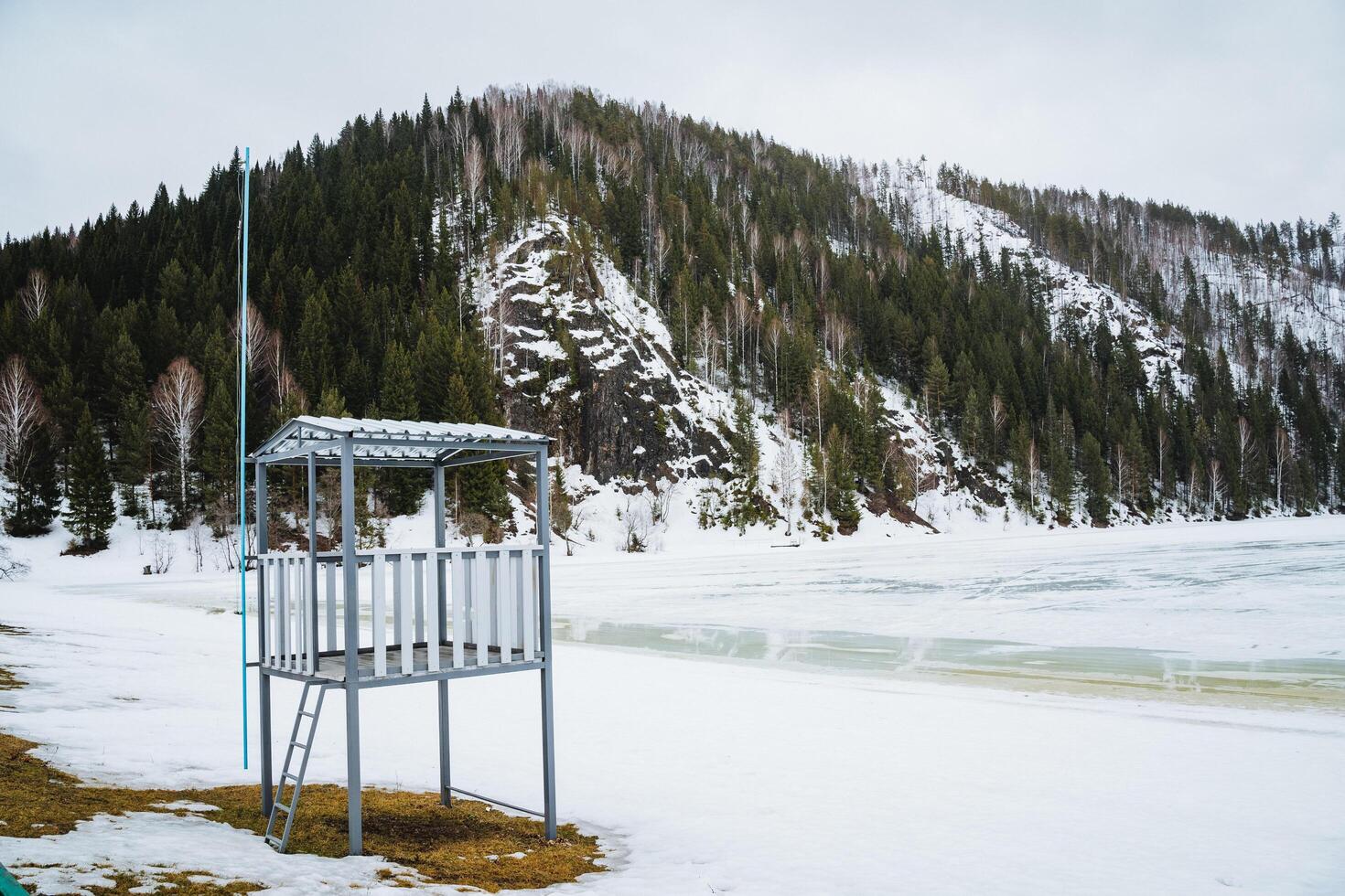 Snowcovered lifeguard tower on shore of freezing lake in mountainous landscape photo