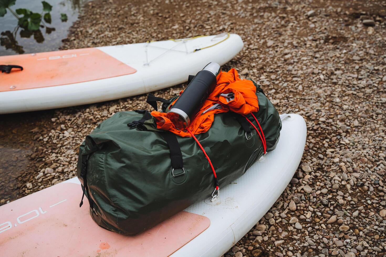 A hermetic bag with things lies on the bow of the SUP board secured with ropes, a thermos with tea on a hike, rafting down the river on a board with an oar, equipment for a water trip. photo
