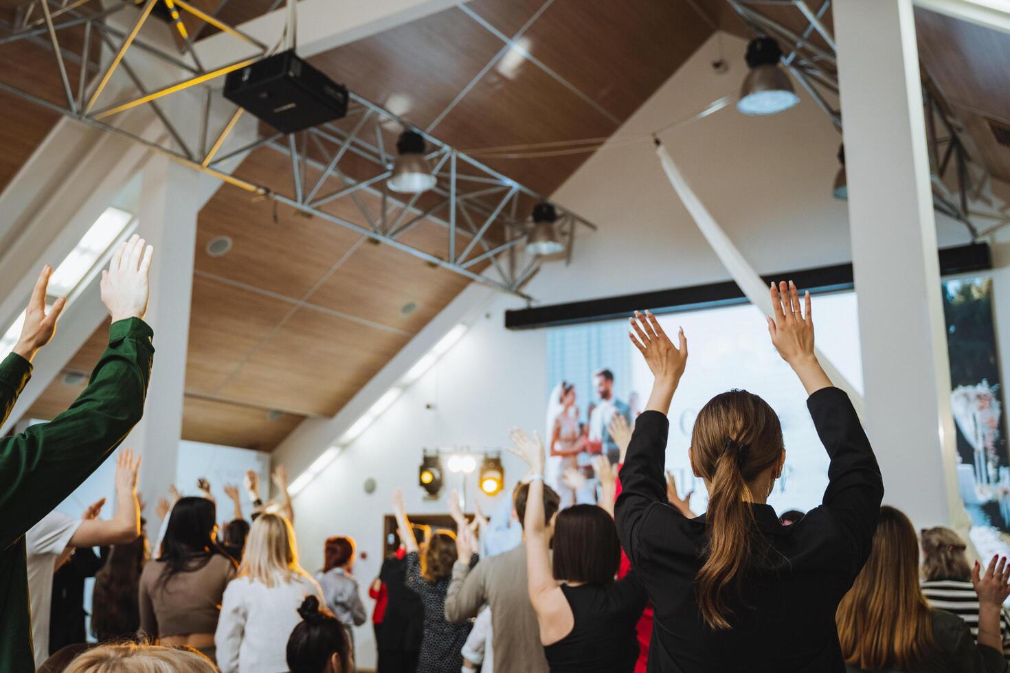 A crowd enjoying an art event, raising hands in a room with a high ceiling photo