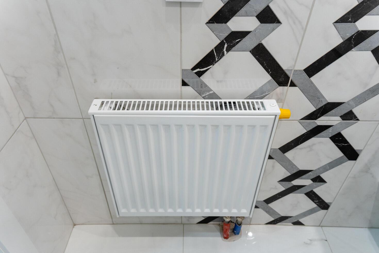 In a beautifully designed bathroom, a pristine white radiator is thoughtfully placed, hanging elegantly on a tiled wall, adding both functionality and aesthetic appeal to the space photo