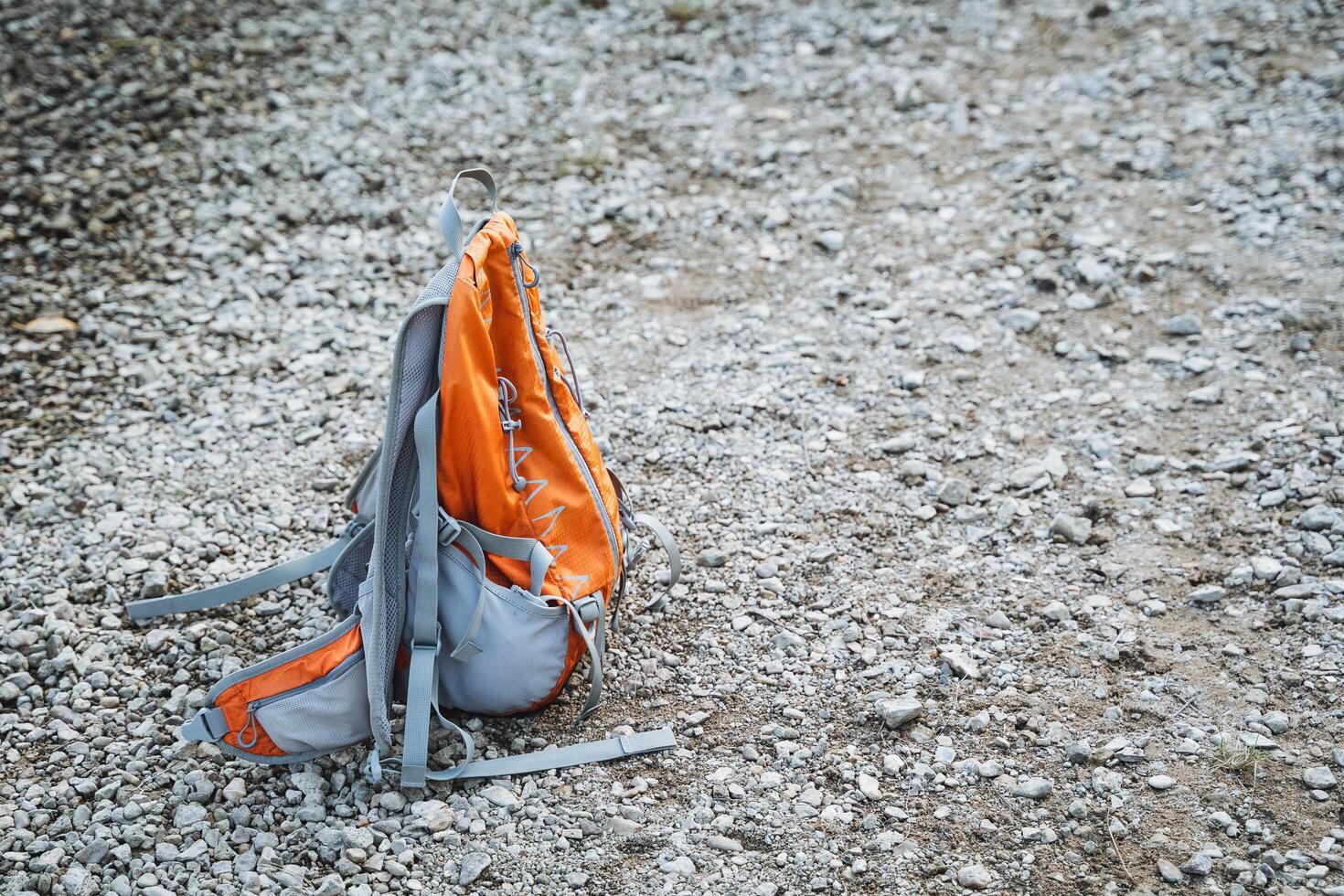 An orange and gray backpack is currently laying on the ground, resting there among other items and debris that may be found in that area, like litter or natural materials photo