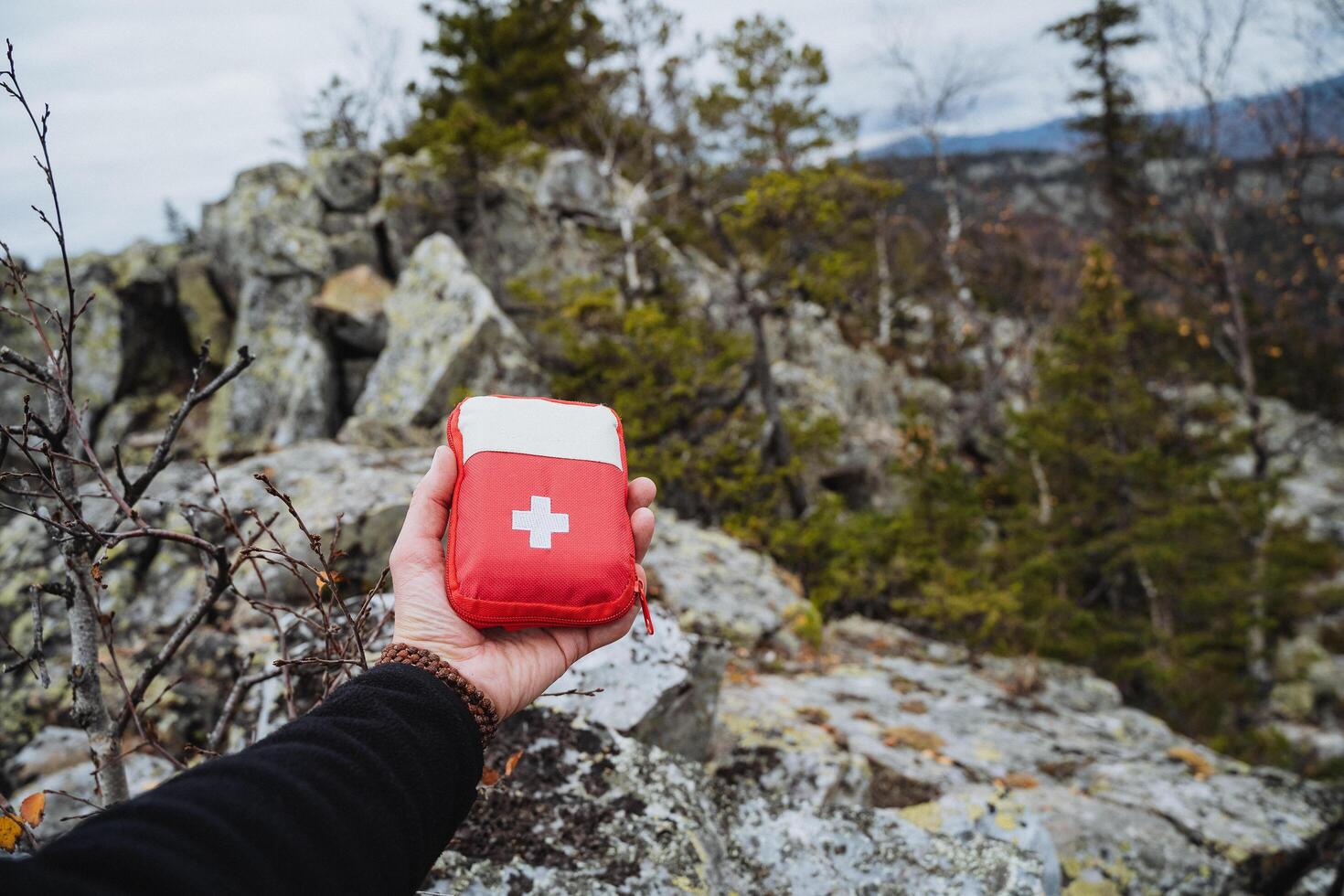 The hand holds a first aid kit on the background of a rock, a tourist first aid kit for hiking in the mountains, a mini cosmetic bag with medicines. photo