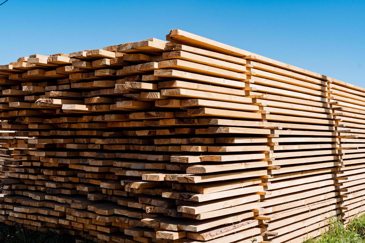 A stack of freshly cut wooden planks sits under a clear blue sky at an outdoor sawmill, showcasing the lumber industry and the processing of raw wood materials photo
