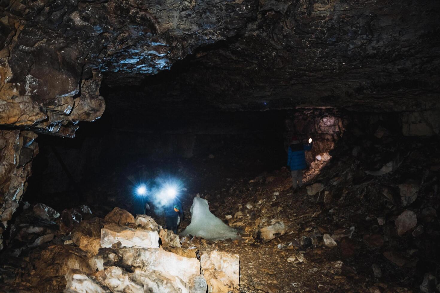 A man stands alone in a dark, eerie cave, firmly holding a powerful flashlight that unveils the breathtaking rock formations and casts intricate, mesmerizing shadows all around him photo