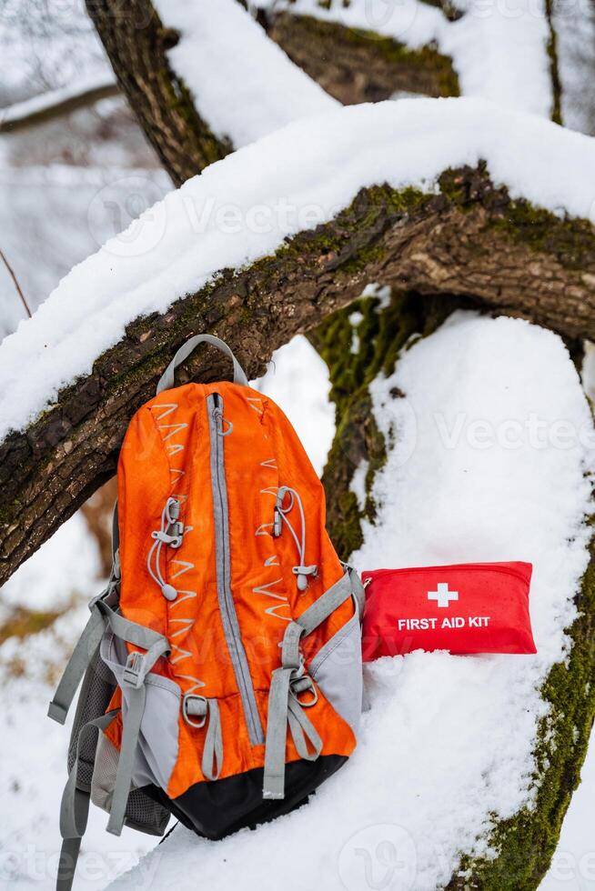 An orange backpack is resting in the cold, white snow, positioned next to a first aid kit that is also visible nearby. The scene captures a contrast between vibrant and cold elements photo