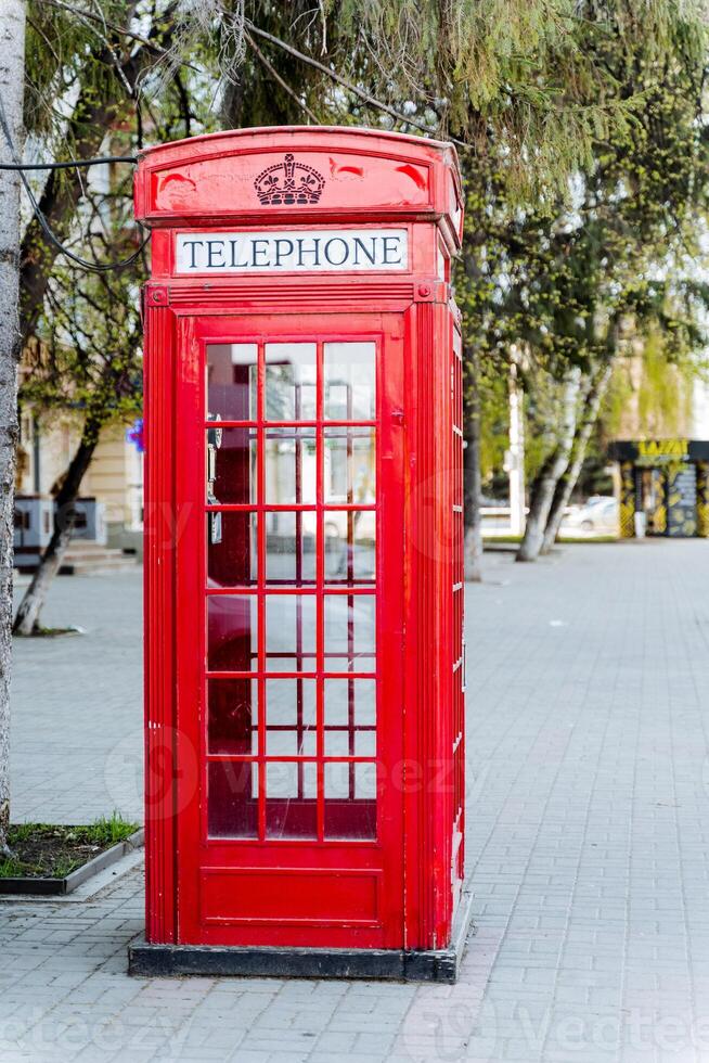 a red telephone booth is sitting on a sidewalk in a park photo